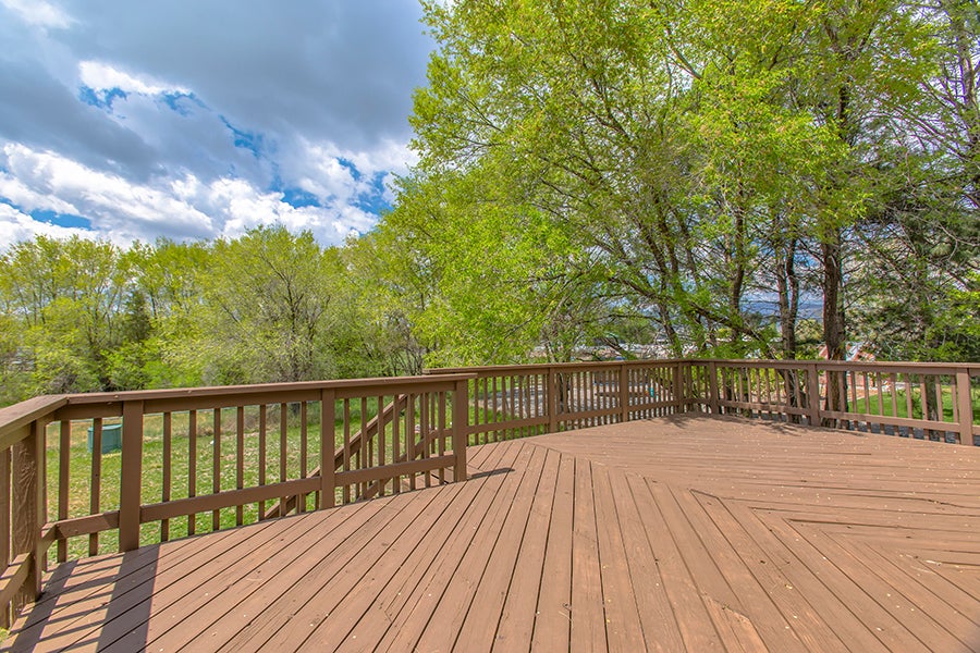 Brown wooden deck overlooking grassy yard and green trees