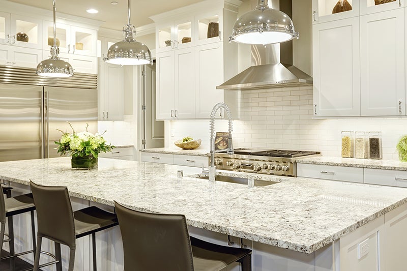 Modern white kitchen with granite island and chrome pendant lights.