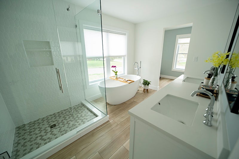 Modern white bathroom with freestanding tub, glass shower, and wood-look tile