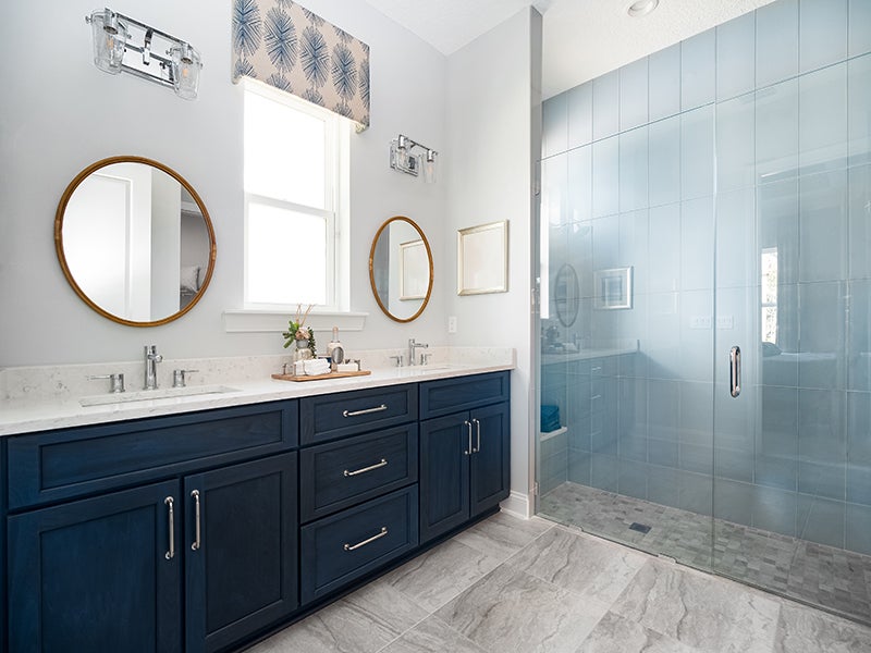 Bathroom with navy double vanity, gray tile floor, and large glass shower.