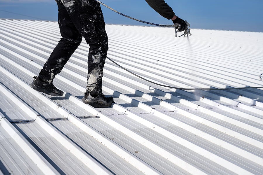 Worker applying coating to metal roof in black and white.