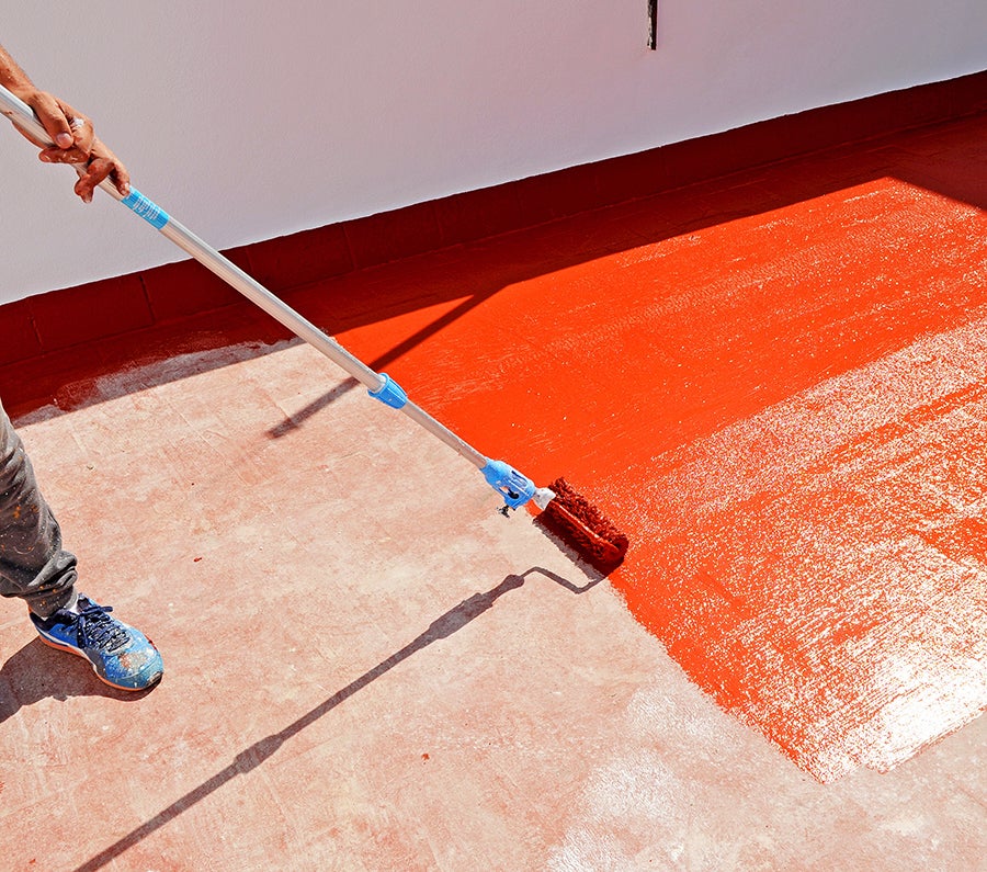 Roller applying orange acrylic coating to flat roof surface.