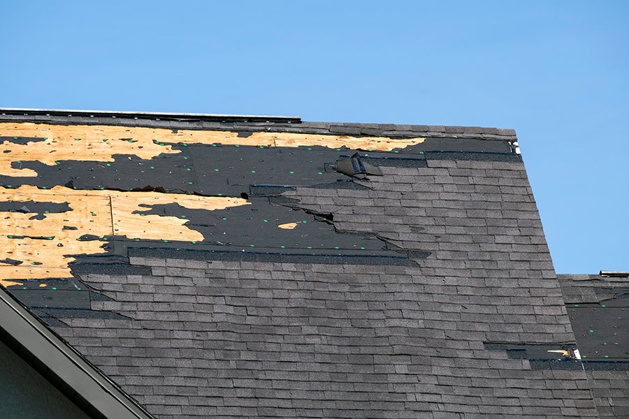 Severely damaged asphalt shingle roof with exposed decking.