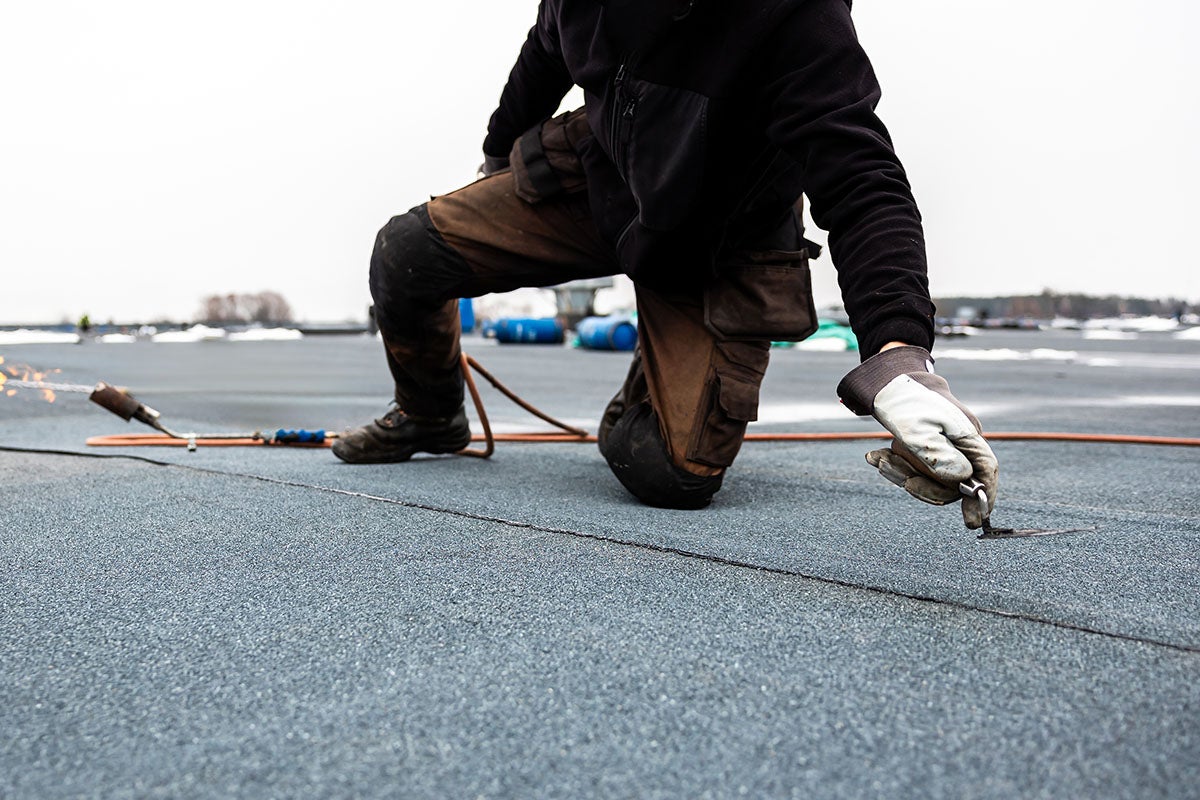 lose-up of worker kneeling on gray flat roof surface