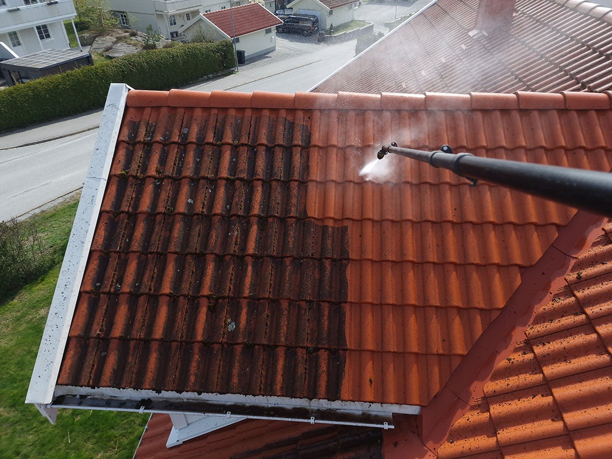 Worker power washing a dirty red tile roof close-up