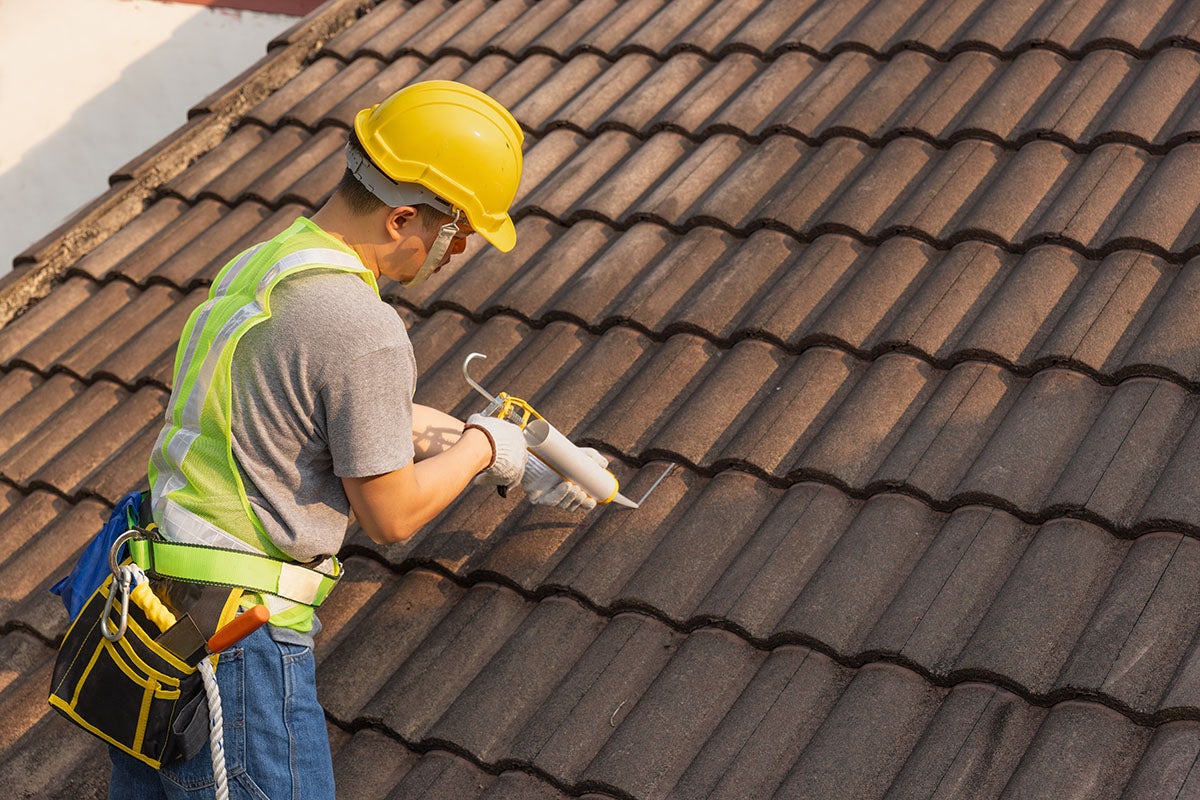 Worker in hard hat performing maintenance on a brown tile roof.
