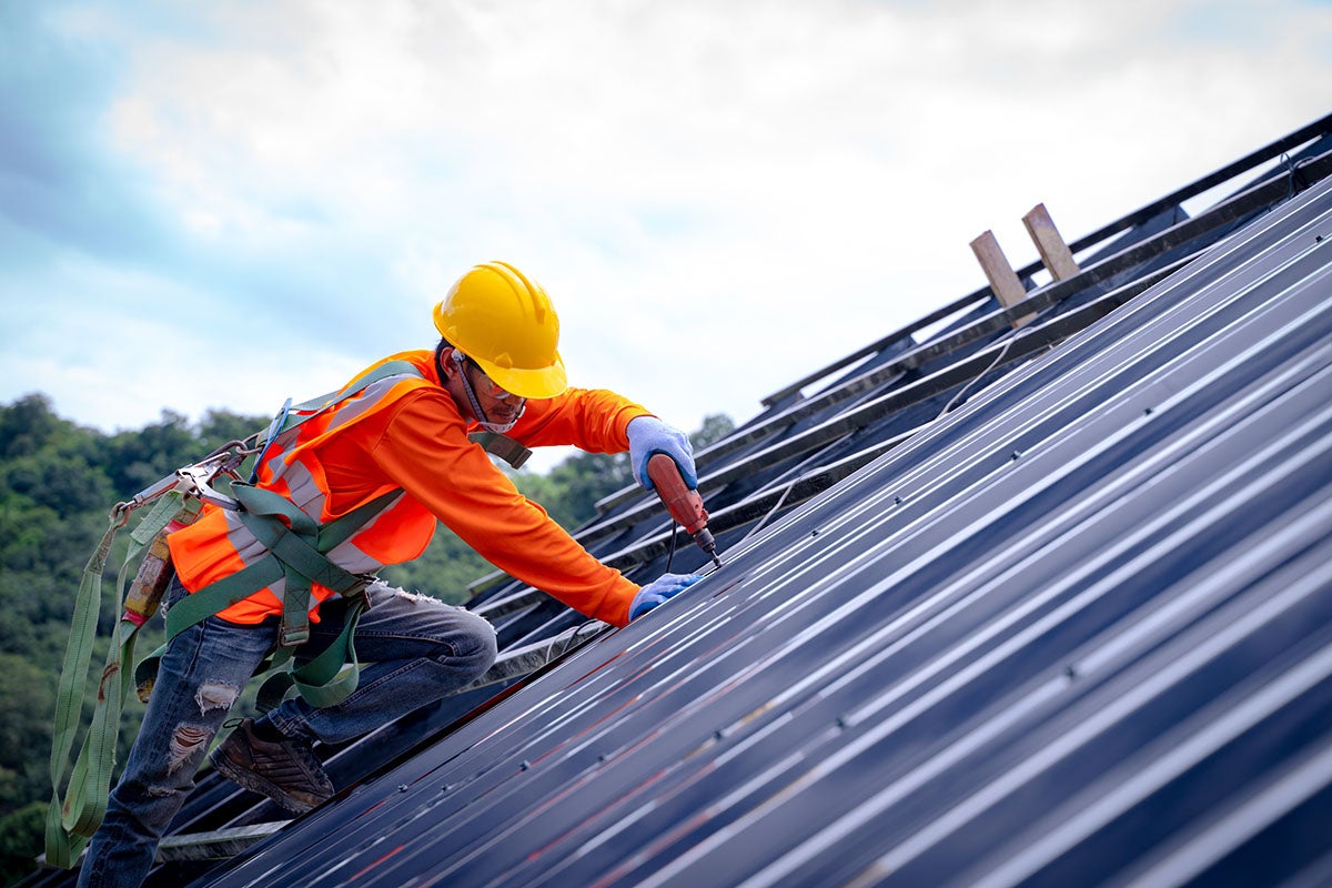 Roofer in orange shirt working on dark metal roof panels