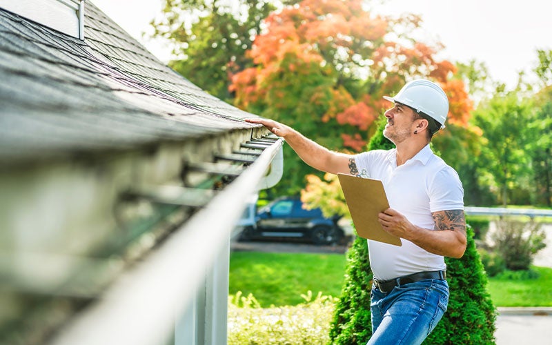 Inspector checking a house gutter with a clipboard
